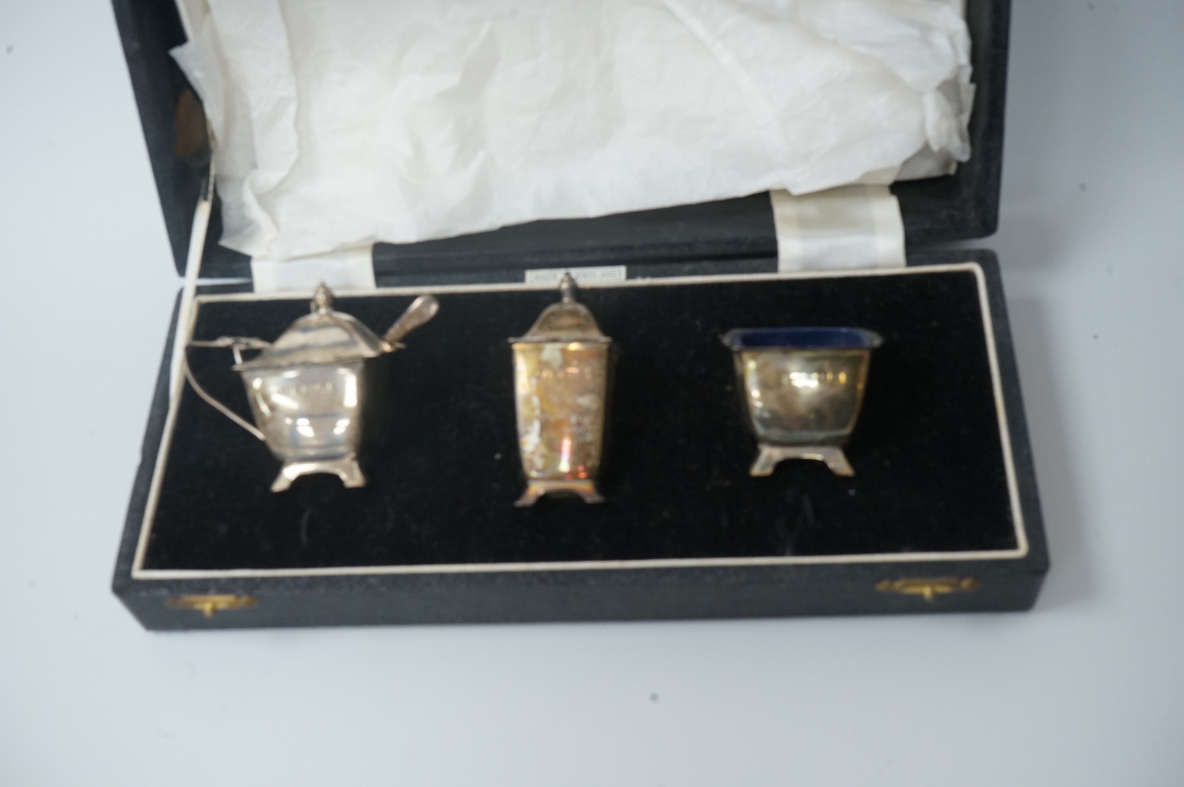 A pair of cased Elizabeth II silver three piece condiment sets, by William Adams Ltd, Birmingham, 1955, one spoon missing.